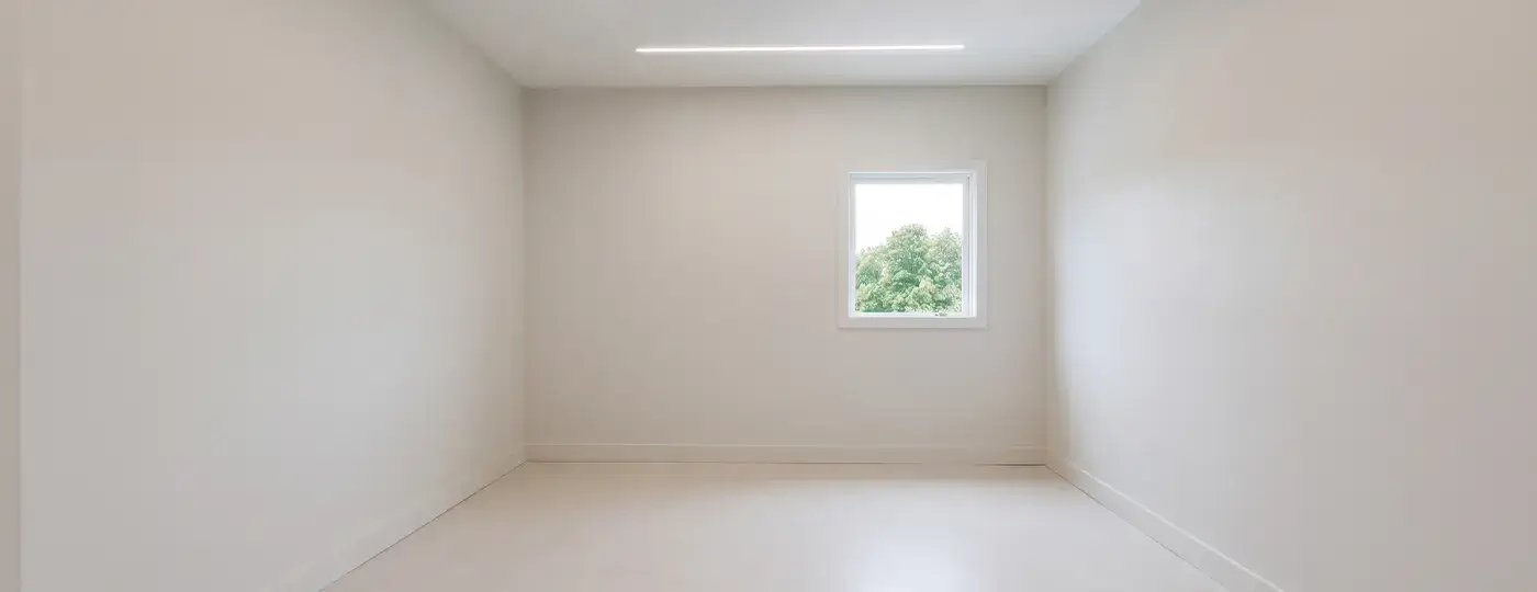Ein leerer, heller Raum mit einer LED-Deckenleuchte und Blick auf Bäume.