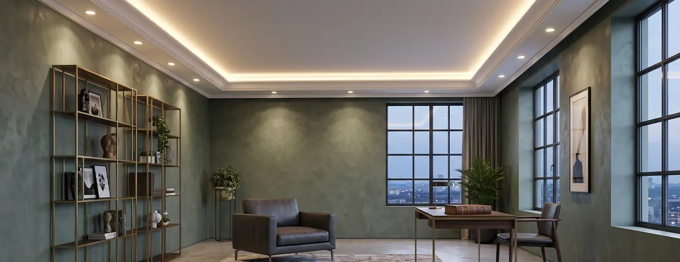 Ein Interieur im organischen Stil mit grünen Wänden, ausgestattet mit einem Schreibtisch, einem Regal und einer abgehängten Decke mit umlaufender LED-Beleuchtung sowie Einbaustrahlern.