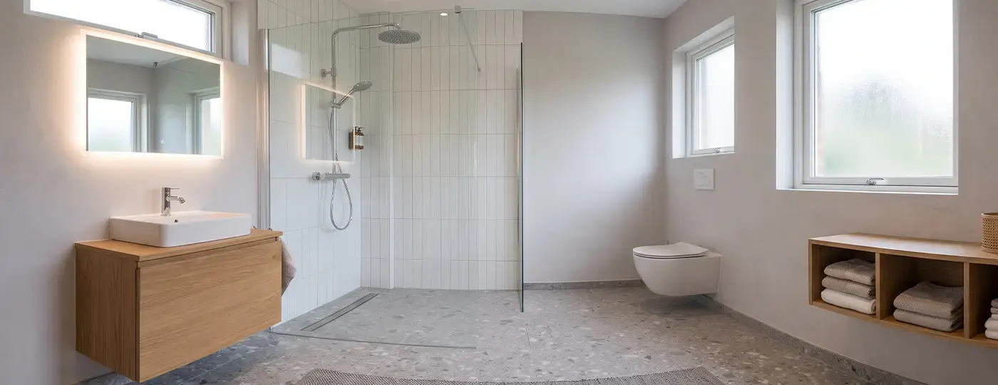 Ein helles, modernes Badezimmer mit bodengleicher Walk-in-Dusche, beleuchtetem LED-Spiegel, wandhängendem Holzwaschtisch und Terrazzoboden.