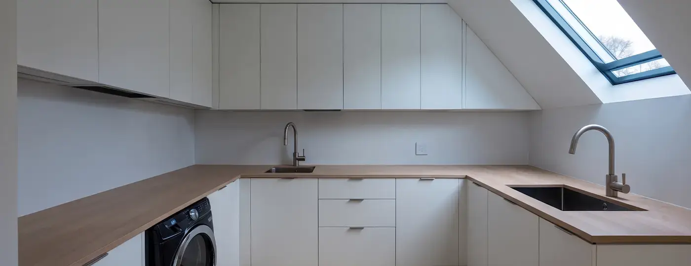 Eine kleine, weiße Dachgeschossküche mit Arbeitsplatten aus Holz und einem Dachfenster.