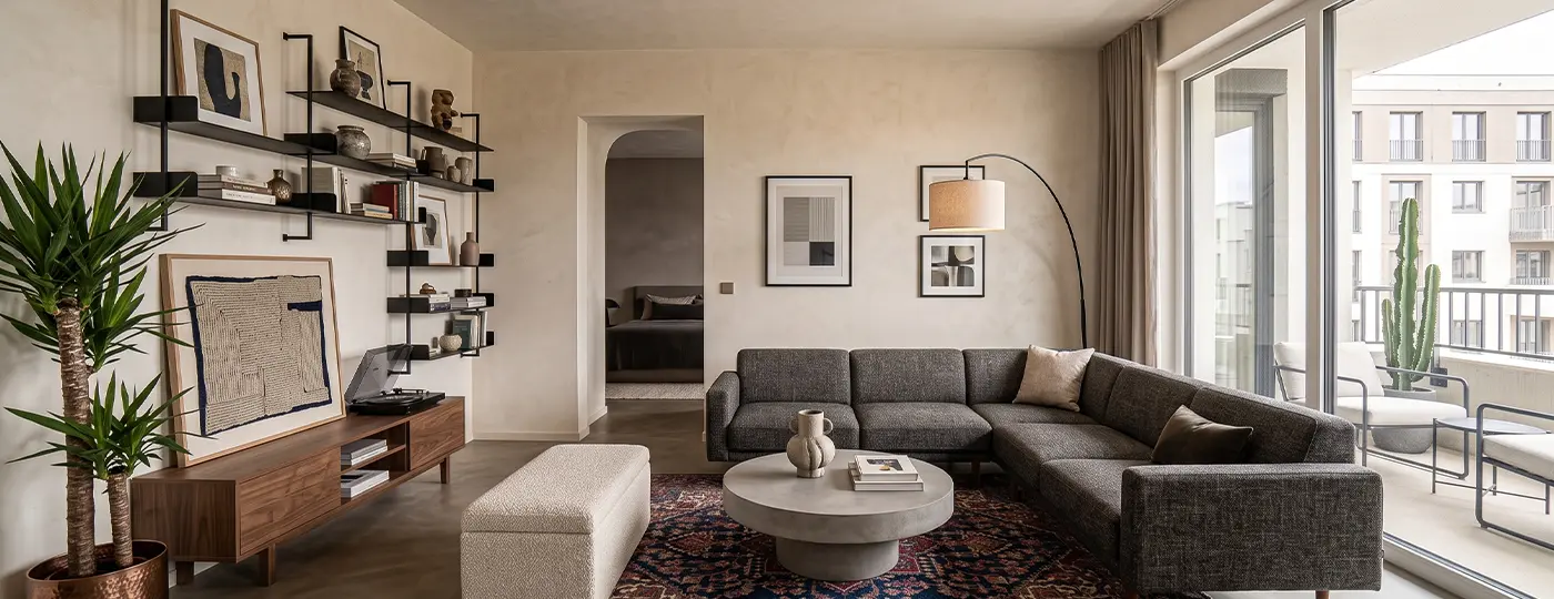 Ein elegantes, gemütliches Wohnzimmer mit einem dunkelgrauen Ecksofa, einem runden Couchtisch, einem Medienmöbel aus Holz und Zugang zum Balkon.