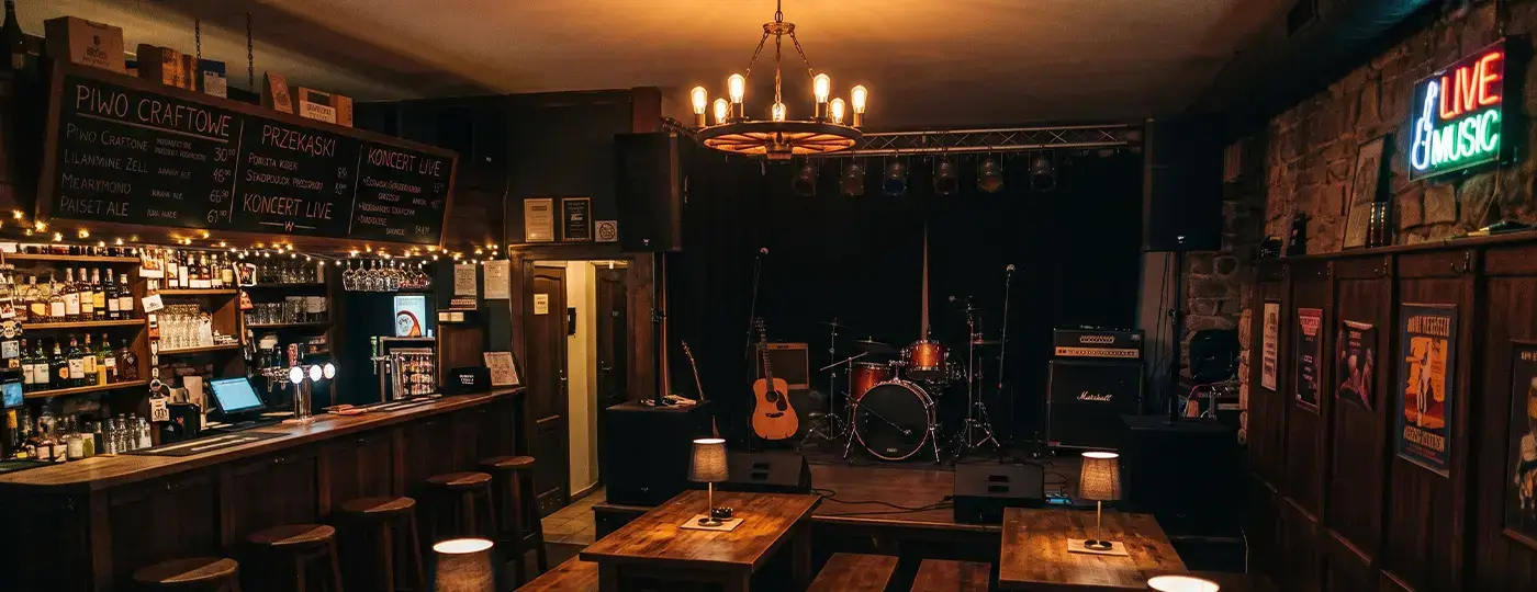 Der Innenraum eines stimmungsvollen Pubs mit einer Theke aus Holz, Tischen und einer Musikbühne, die mit Schlagzeug und Verstärkern ausgestattet ist.