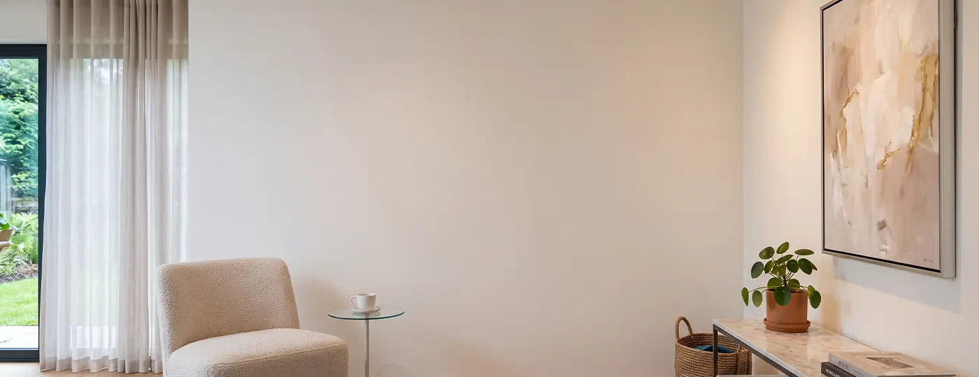 Eine Frau in einem hellen Anzug und mit Schutzhelm steht in einem modernen Wohnzimmer mit Designer-Deckenbeleuchtung und hält ein Tablet sowie ein Gebäudemodell in der Hand.