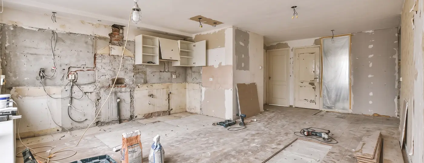 Eine Wohnung, die umfassend renoviert wird: Küchenelemente sind teilweise demontiert, Wände freigelegt und Werkzeuge auf dem Boden verstreut.