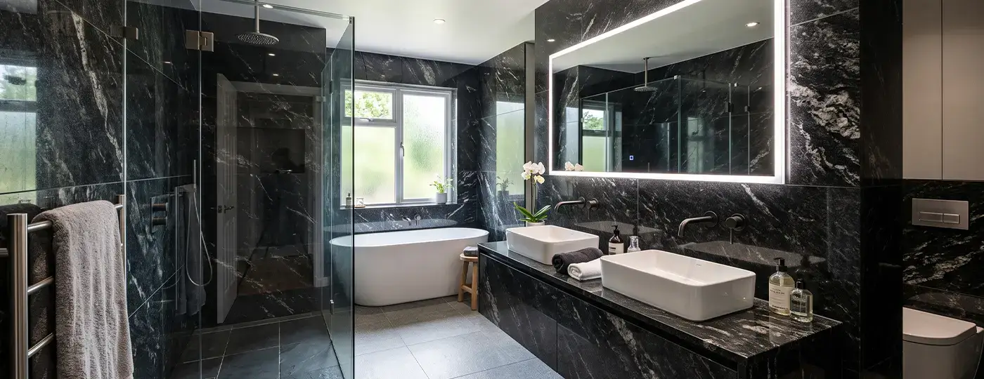 Dunkles, luxuriöses Badezimmer aus Granit mit Badewanne, beleuchtetem Spiegel und zwei Waschbecken.