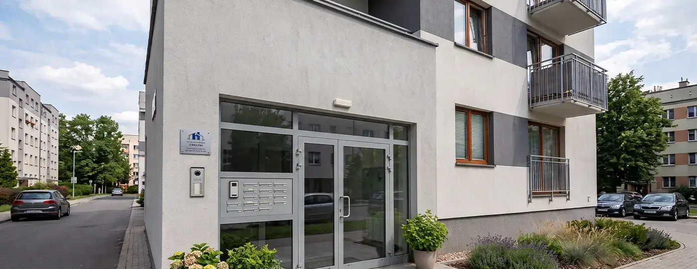 Moderner, verglaster Eingang zum Treppenhaus eines Mehrfamilienhauses mit grauen Türrahmen und Gegensprechanlage.