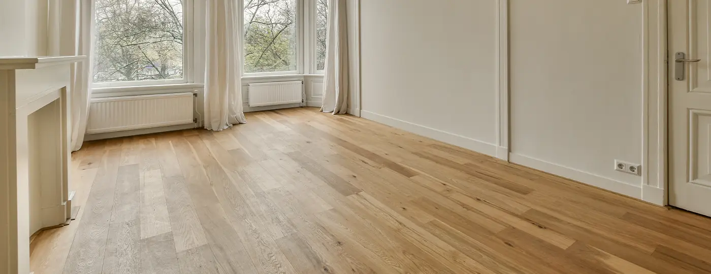 Geräumiger, leerer Innenraum mit weißen Wänden, einem Erkerfenster und einem fertiggestellten Boden aus hellen Holzdielen.