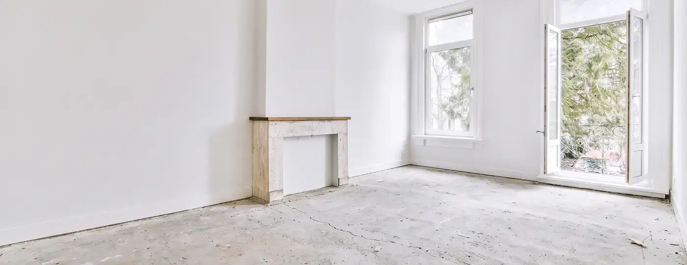 Heller, leerer Rohbau mit weißen Wänden, Betonestrich, dekorativem Kaminportal und geöffneten Balkontüren.