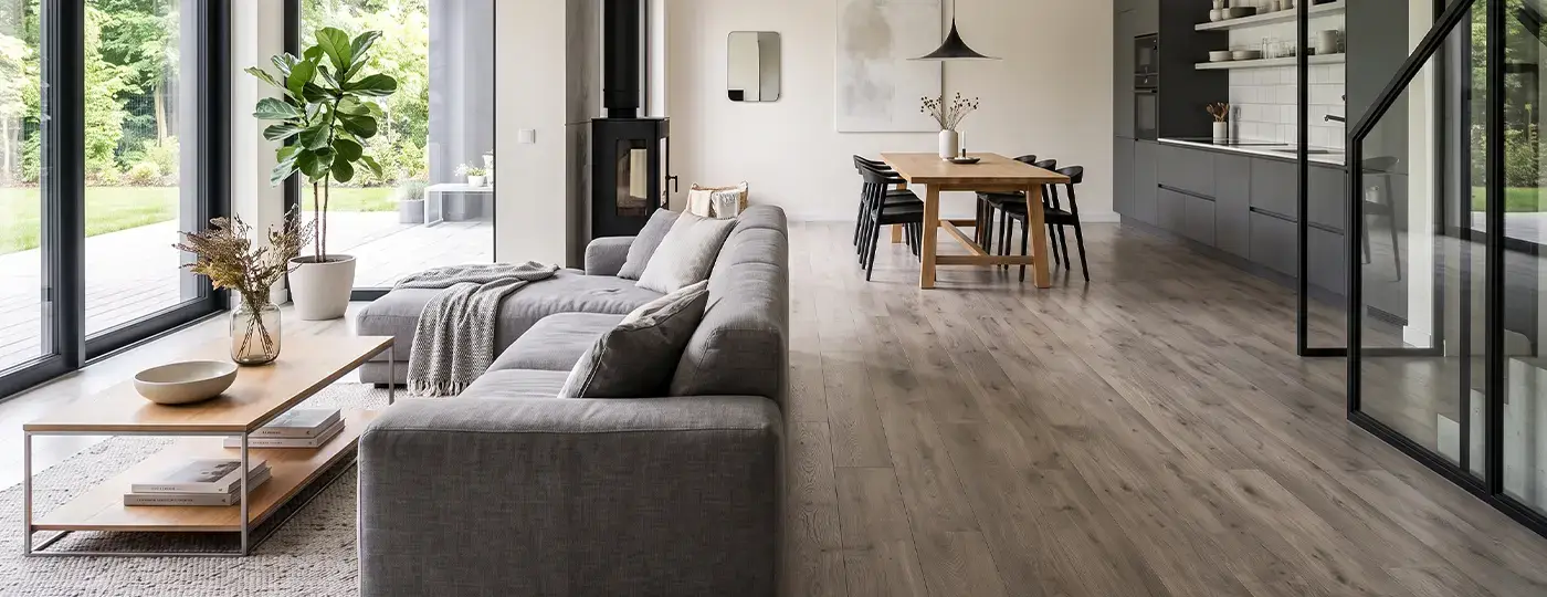 Ein helles, offenes Wohnzimmer mit dunkelgrauem Sofa, Holzboden, Kochnische und Essbereich.