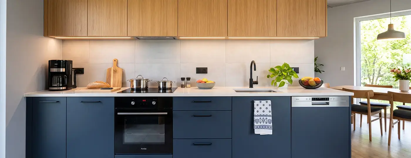 Moderne Küche mit dunkelblauen Unterschränken, Hängeschränken aus Holz, heller Arbeitsplatte und weißen Wandfliesen.