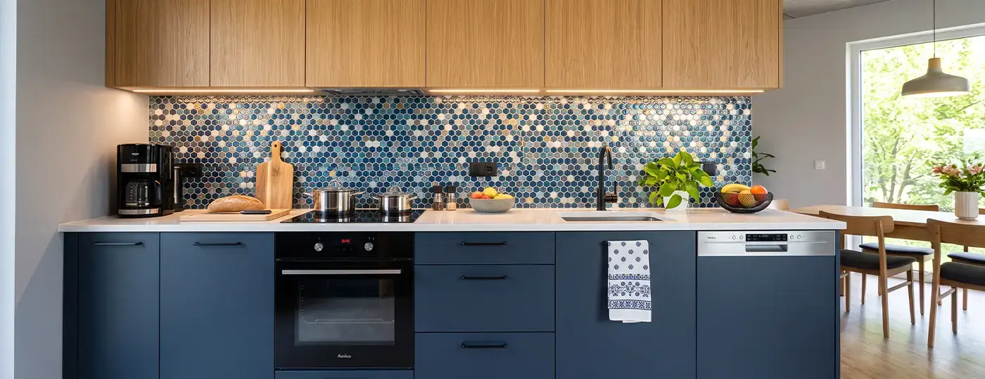 Moderne Küche mit dunkelblauen Unterschränken, Hängeschränken aus Holz, heller Arbeitsplatte und blauem Wandmosaik.
