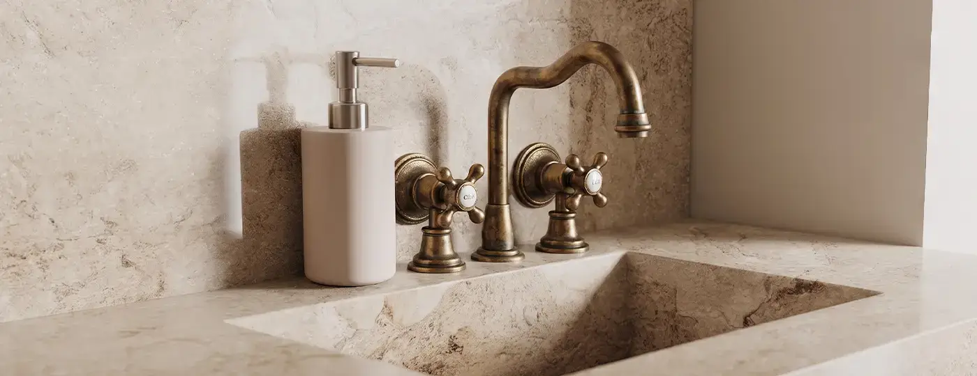 3-Loch-Waschtischarmatur aus patiniertem Messing im Retro-Stil mit Kreuzgriffen, montiert an einem in die Waschtischplatte eingelassenen Steinwaschbecken.