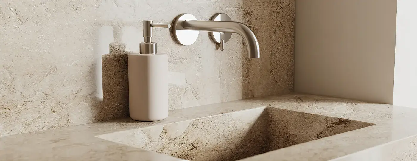 Eine minimalistische Waschtischarmatur aus gebürstetem Stahl zur Unterputz-Wandmontage, positioniert über einem auf einer gemeinsamen Waschtischplatte stehenden Steinwaschbecken.