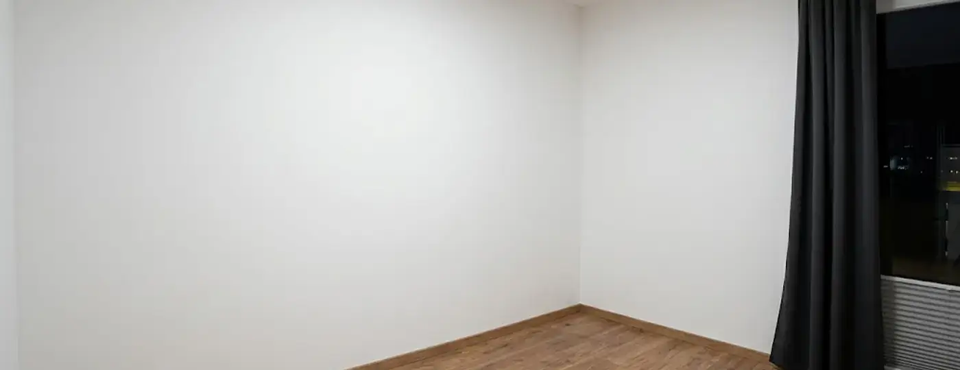 Ein leerer Raum mit weißen Wänden, Holzboden und einem dunklen Vorhang, vorbereitet als Gaming-Zimmer.
