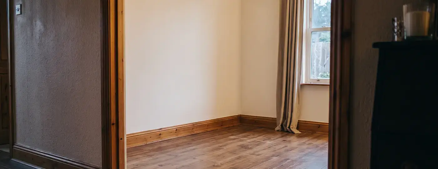 Ein leerer Raum mit hellen Wänden, Holzboden und einem Fenstervorhang.