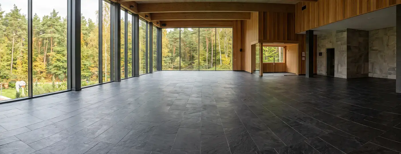 Großer, leerer Poolbereich mit Panoramafenstern, Blick auf den Wald und dunklem Bodenbelag.