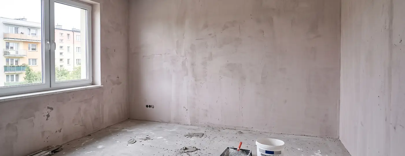 Ein leerer Raum mit Rohputz und einem Eimer auf dem Boden.