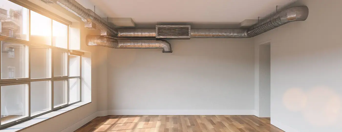 Heller Raum mit freiliegenden, abgehängten Lüftungsrohren unter der Decke.